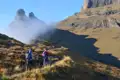 Zwei Wanderer auf einem Bergpfad.  Felsige Gipfel und Nebel sind im Hintergrund sichtbar.