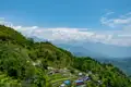 Panoramablick auf ein Bergdorf mit terrassierten Feldern und den schneebedeckten Himalaya-Gipfeln im Hintergrund.
