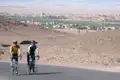 Zwei Radfahrer auf einer Radtour in einer Wüstenlandschaft. Im Hintergrund ist eine Stadt sichtbar.