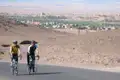 Zwei Radfahrer auf einer Radtour durch eine Wüstenlandschaft. Sie nähern sich einer Stadt im Hintergrund.