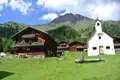 Traditionelle Holzhäuser und eine Kapelle in einer Berglandschaft.
