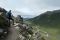 Wanderer auf einem Bergpfad mit Blick auf ein Tal und eine Straße.
