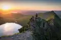 Wanderer auf einem Berggipfel mit Blick auf den Sonnenuntergang und einen See.
