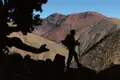 Silhouette eines Wanderers mit Rucksack und Wanderstöcken in einer bergigen Landschaft.