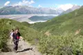 Wanderer auf einem Bergpfad mit Blick auf einen Gletscher und schneebedeckte Berge im Hintergrund.