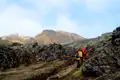 Wandergruppe auf einem Pfad durch ein Lavafeld mit Bergen im Hintergrund.
