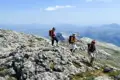 Drei Wanderer auf einem felsigen Bergpfad mit Blick auf die Berglandschaft.