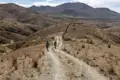 Zwei Wanderer auf einem Bergpfad in einer trockenen, bergigen Landschaft.