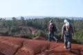 Zwei Wanderer erkunden die Landschaft auf einem Wanderweg mit markantem roten Boden.