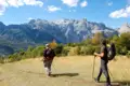 Zwei Wanderer mit Wanderstöcken auf einem Bergpfad mit einer Bergkette im Hintergrund.