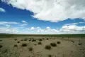 Offene Landschaft mit spärlicher Vegetation und blauem Himmel mit Wolken.