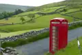 Eine klassische rote britische Telefonzelle an einer Landstraße in einer hügeligen Landschaft.