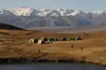 Wanderer zelten in einer hochgelegenen Landschaft mit einem See im Vordergrund und schneebedeckten Bergen im Hintergrund.