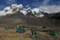 Basislager mit Zelten in einer hochgelegenen Berglandschaft. Schneebedeckte Gipfel und Gletscher im Hintergrund.