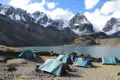 Zeltlager am Ufer eines Bergsees inmitten einer Hochgebirgslandschaft mit schneebedeckten Gipfeln.