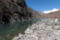 Klares Wasser eines Bergsees im Himalaya, umgeben von Felsen und mit schneebedeckten Gipfeln im Hintergrund.