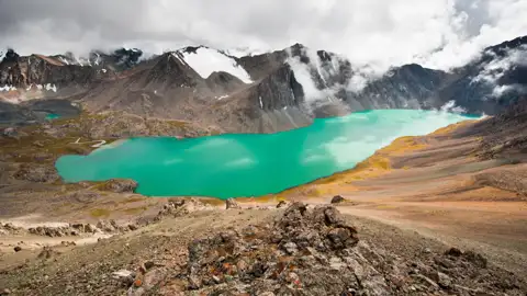 Türkisfarbener See in den Bergen mit schneebedeckten Gipfeln im Hintergrund.