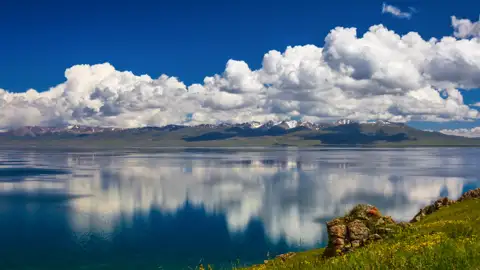 Ruhiger See mit Spiegelung der schneebedeckten Berge und Wolken.