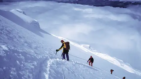 Bergsteiger beim Aufstieg eines verschneiten Berges, gesichert durch ein Seil.