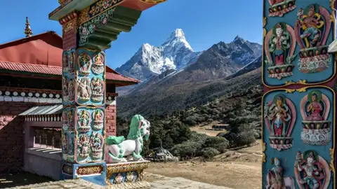 Blick durch ein kunstvoll verziertes Tor eines buddhistischen Tempels auf die schneebedeckten Himalaya-Gipfel.