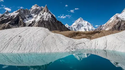 Ein Gletschersee reflektiert die umliegenden schneebedeckten Gipfel.