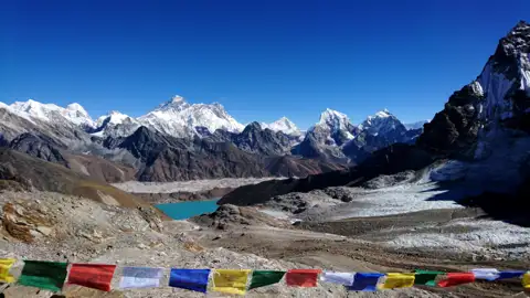 Gebetsfahnen im Vordergrund mit Blick auf einen türkisfarbenen Gletschersee und schneebedeckte Gipfel des Himalayas.