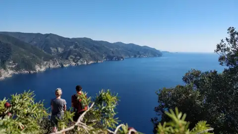 Zwei Wanderer auf einem Aussichtspunkt mit Blick auf das Meer und die Küste.