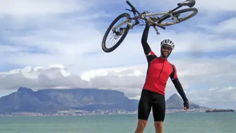 Erfolgreicher Abschluss einer Radtour: Radfahrer mit erhobenem Fahrrad vor dem Tafelberg.