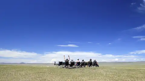 Reisende entspannen sich in Campingstühlen und genießen die Aussicht auf die weite Landschaft.