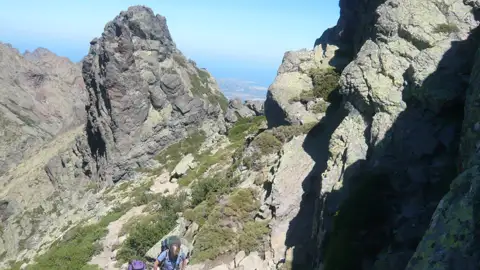 Wanderer auf einem Bergpfad mit felsigen Gipfeln im Hintergrund.