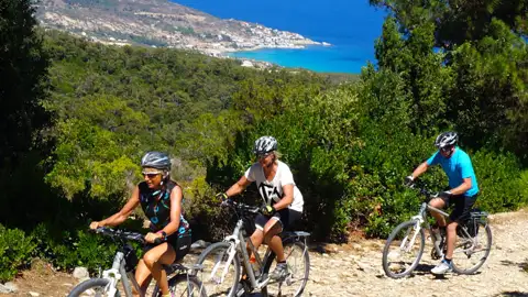 Drei Radfahrer genießen eine Radtour auf einem Küstenweg mit Blick auf das Meer und die Hügel.