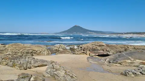 Felsiger Küstenabschnitt mit Blick auf einen Berg am Meer.