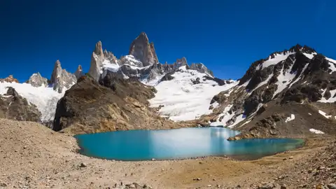 Panoramablick auf einen türkisblauen See, umgeben von schneebedeckten Bergen und Gletschern.