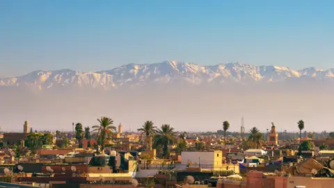 Blick auf die Dächer von Marrakesch mit dem schneebedeckten Atlasgebirge im Hintergrund.