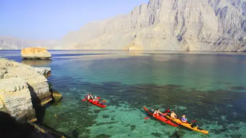 Kajaks im türkisfarbenen Wasser, umgeben von felsigen Klippen und Bergen.