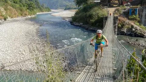 Radfahrer auf einer Hängebrücke über einen Fluss.