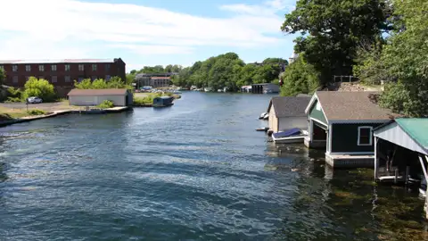 Bootshäuser am Flussufer mit Gebäuden im Hintergrund.