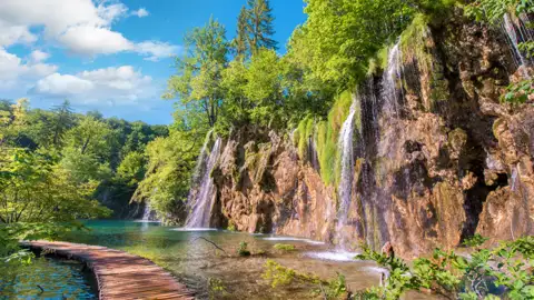 Spektakuläre Wasserfälle, die über eine Felswand in einen türkisfarbenen See im Nationalpark kaskadieren. Ein Holzsteg schlängelt sich durch das flache Wasser und bietet Zugang zu dieser atemberaubenden Naturkulisse.