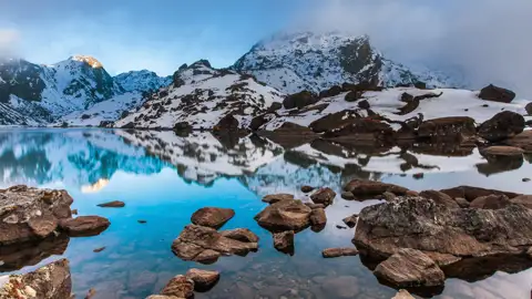 Ruhiger Bergsee mit Spiegelung der umliegenden schneebedeckten Berglandschaft.