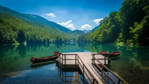 Ruhiger See mit Booten und Steg inmitten einer bewaldeten Hügellandschaft.