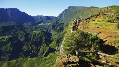 Wanderer genießen die Aussicht von einem Bergpfad auf ein üppiges grünes Tal.