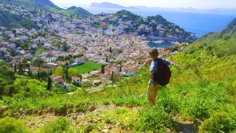 Wanderer auf einem Hügel mit Blick auf eine Küstenstadt und das Meer.