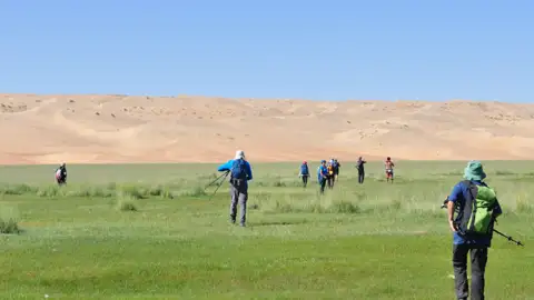 Wandergruppe in einer grünen Oase vor dem Hintergrund von Sanddünen.