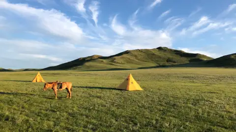 Pferd und Zelte in einer grünen Hügellandschaft.
