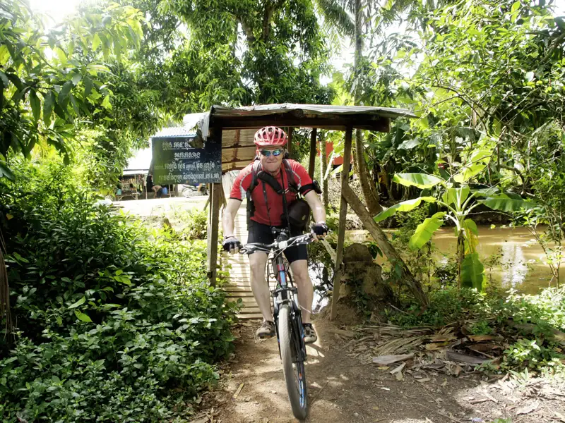 Radfahrer auf einer Holzbrücke inmitten tropischer Vegetation.