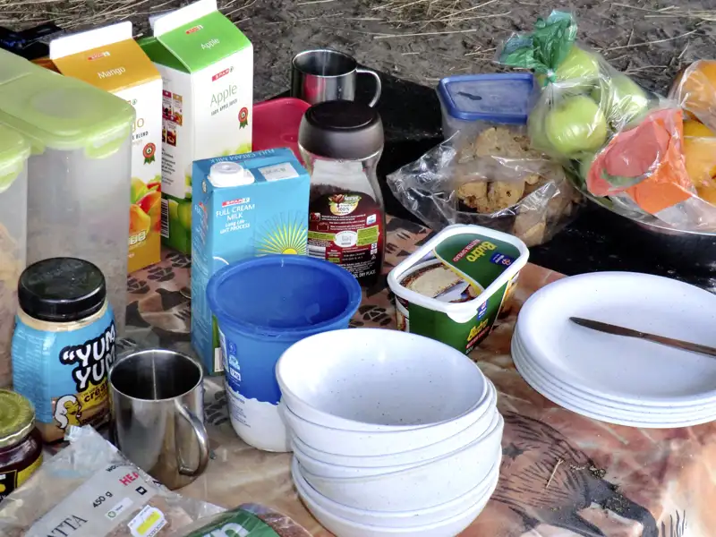 Frühstücksvorbereitungen mit Milch, Saft, Obst, Brot und Butter.