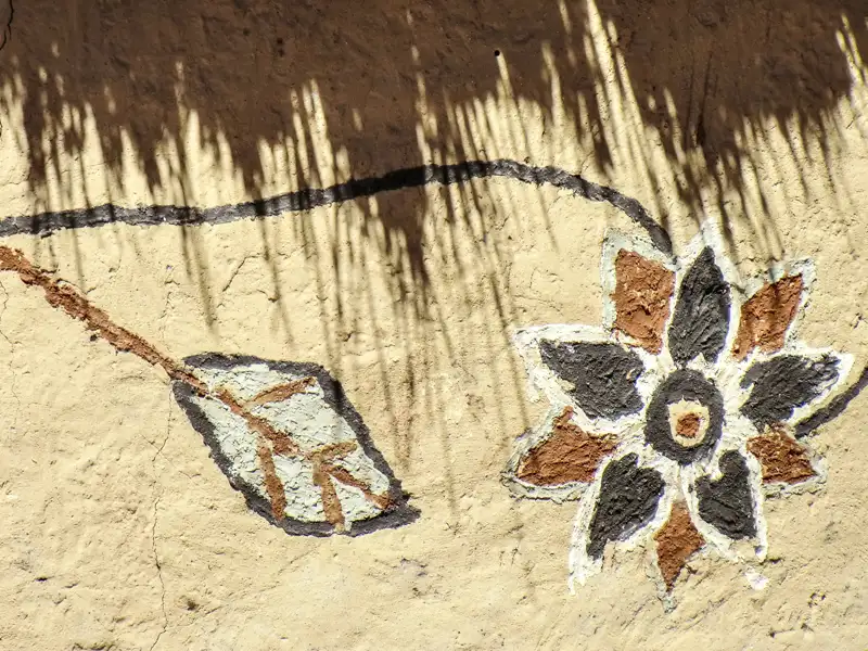 Traditionelle Wandmalerei mit floralen Motiven an einer Lehmwand.
