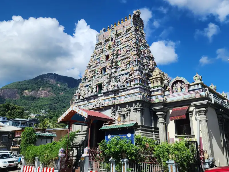 Hindu-Tempel mit detaillierten Verzierungen und bunten Figuren vor einem bewaldeten Berghang.