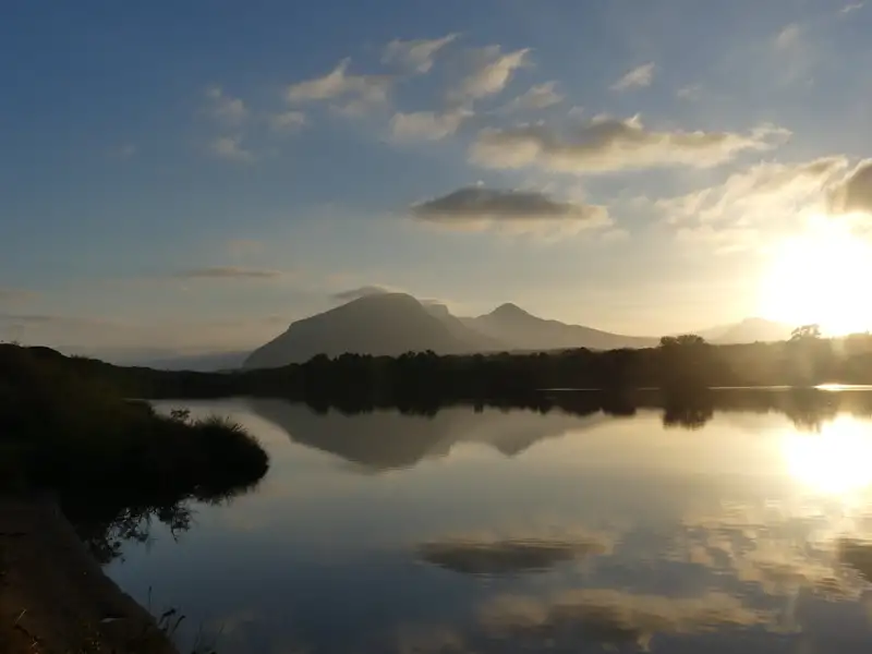 Sonnenaufgang über einem See, die Berge spiegeln sich im Wasser.