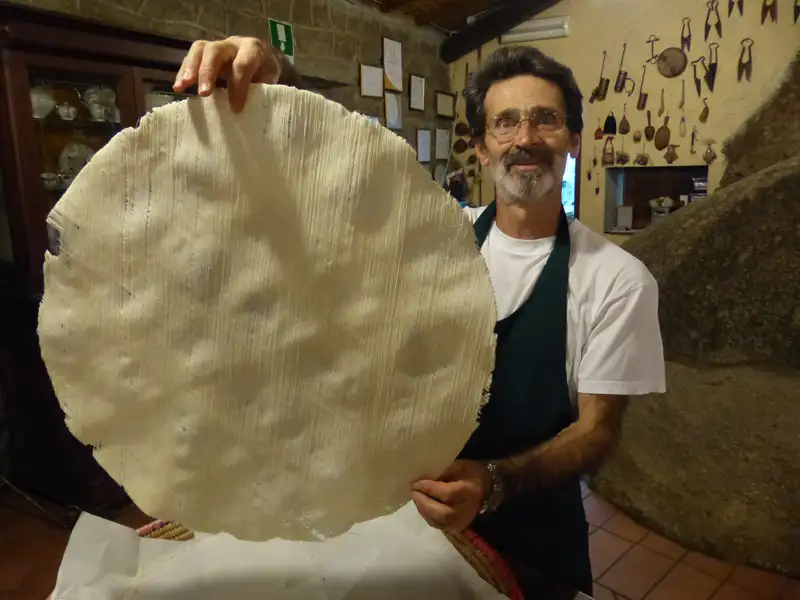 Präsentation eines großen, runden Teigfladens, möglicherweise Teil einer lokalen Spezialität.